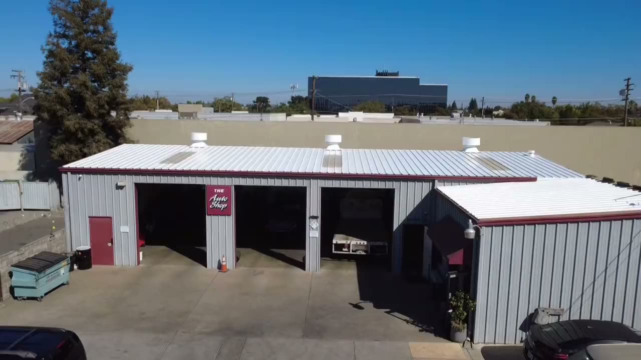 Drone pushing in over a commercial shop's metal roof coated white, ending close on the vents